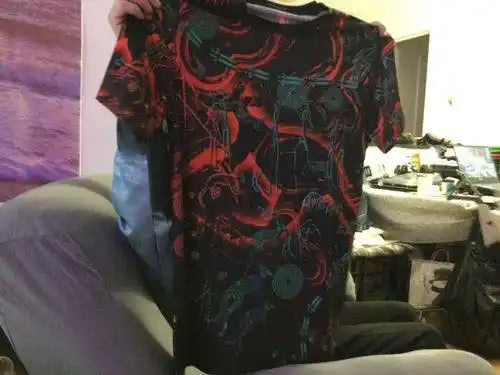 Person holding a black t-shirt with red and blue designs in a casual setting.