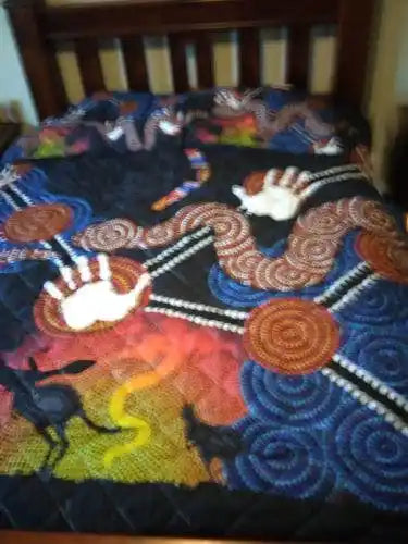 Colorful quilt with Aboriginal art design on a wooden bed frame.