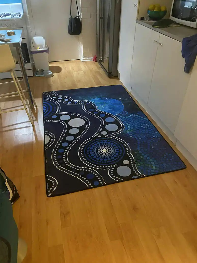 Decorative blue and black patterned rug on a wooden floor in a kitchen.