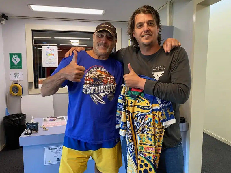 Two men posing together in a room with a colorful towel.