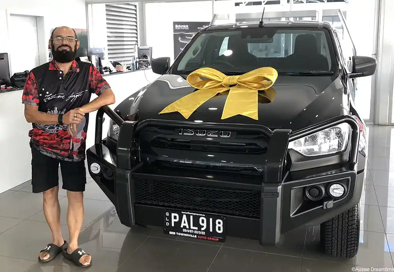 Man standing next to a black Isuzu truck with a yellow bow in a showroom.