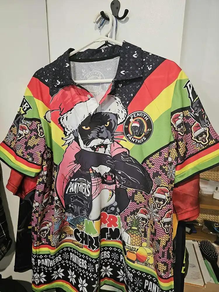 Colorful shirt with graphic designs and text on a hanger against a white wall.