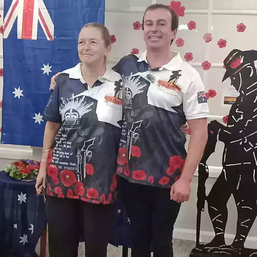 Two people wearing matching shirts with a design of a soldier and poppies, standing in front of an Australian flag.