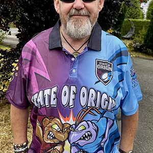 Man wearing a 'State of Origin' themed polo shirt with cartoon characters outdoors.