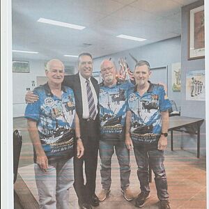 Four men in matching blue shirts with a pattern, standing together in an indoor setting.