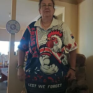 Person wearing a colorful shirt with a rooster design and text indoors.