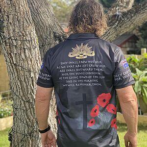 Person wearing a shirt with text and poppy designs, standing outdoors near a tree.