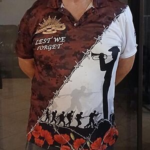 Person wearing a shirt with a design featuring soldiers and barbed wire, with text 'Lest We Forget'.