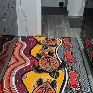 Decorative rug with Aboriginal art design on a floor.