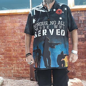 Person wearing a black t-shirt with a graphic design and text in front of a brick wall.