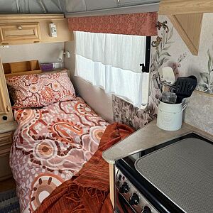 Small kitchenette inside a recreational vehicle with a bed and cooking area.