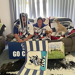 Two people sitting on a couch with a dog, surrounded by sports-themed decor.
